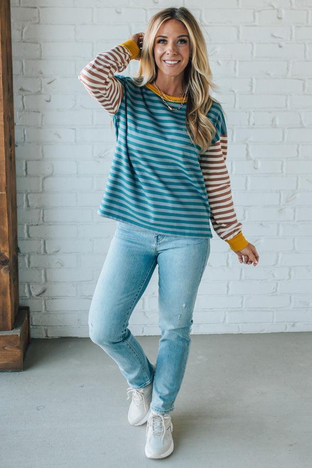 Woman wearing a striped shirt and jeans standing against a white brick wall.
