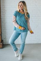 Woman wearing a striped shirt and jeans standing against a white brick wall.