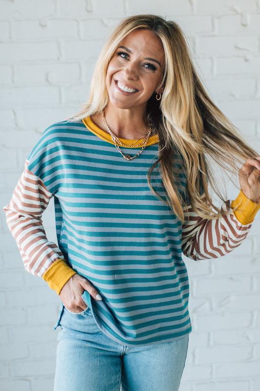 Woman wearing a striped long-sleeve shirt with colorful cuffs against a white brick wall.