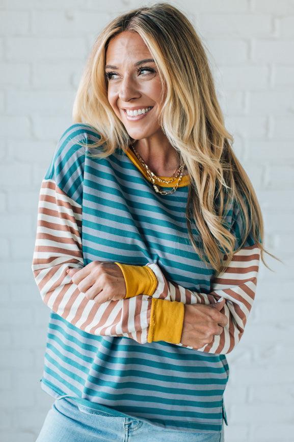 Woman wearing a striped shirt with yellow cuffs and collar against a white brick wall.