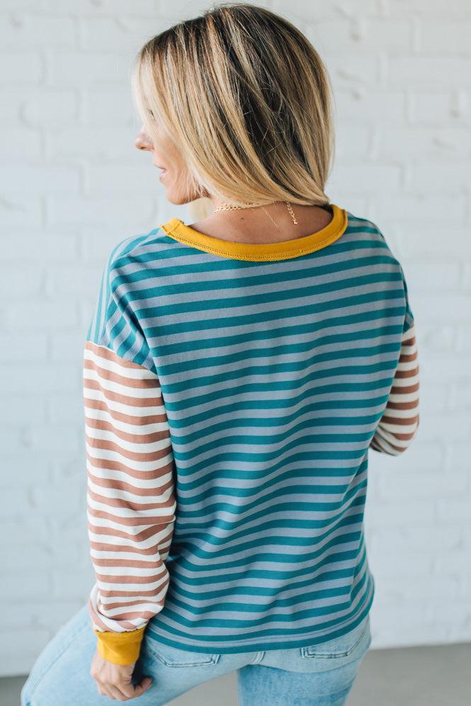 Woman wearing a striped long-sleeve shirt with a yellow trim against a white wall.