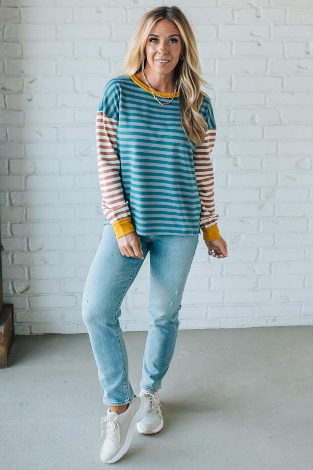 Woman wearing a striped sweater and jeans against a white brick wall.