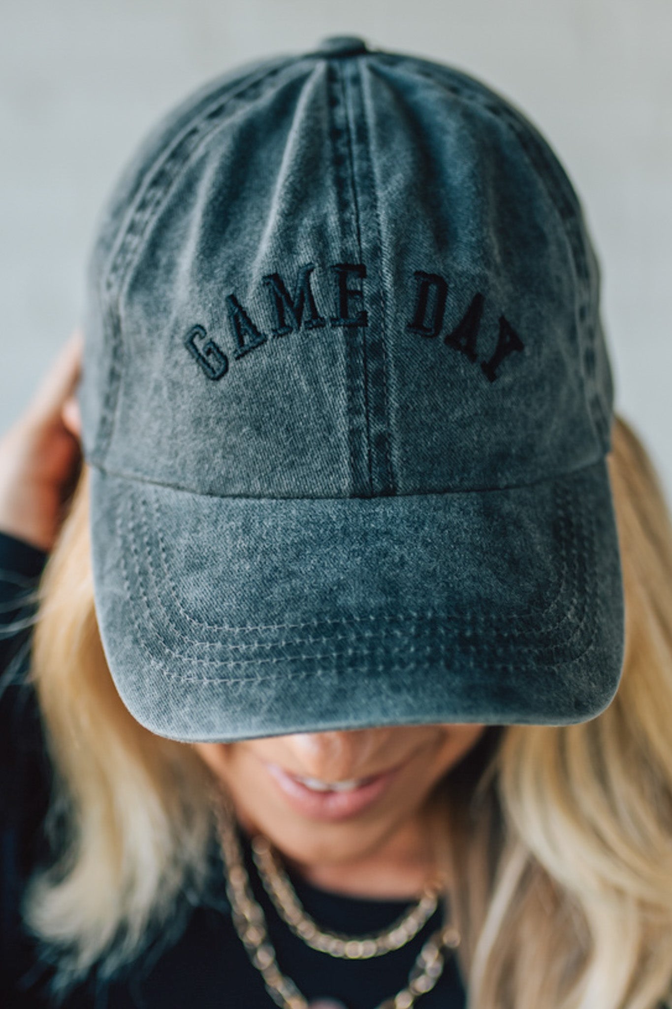Blue denim cap with 'GAME DAY' text worn by a person with blonde hair.