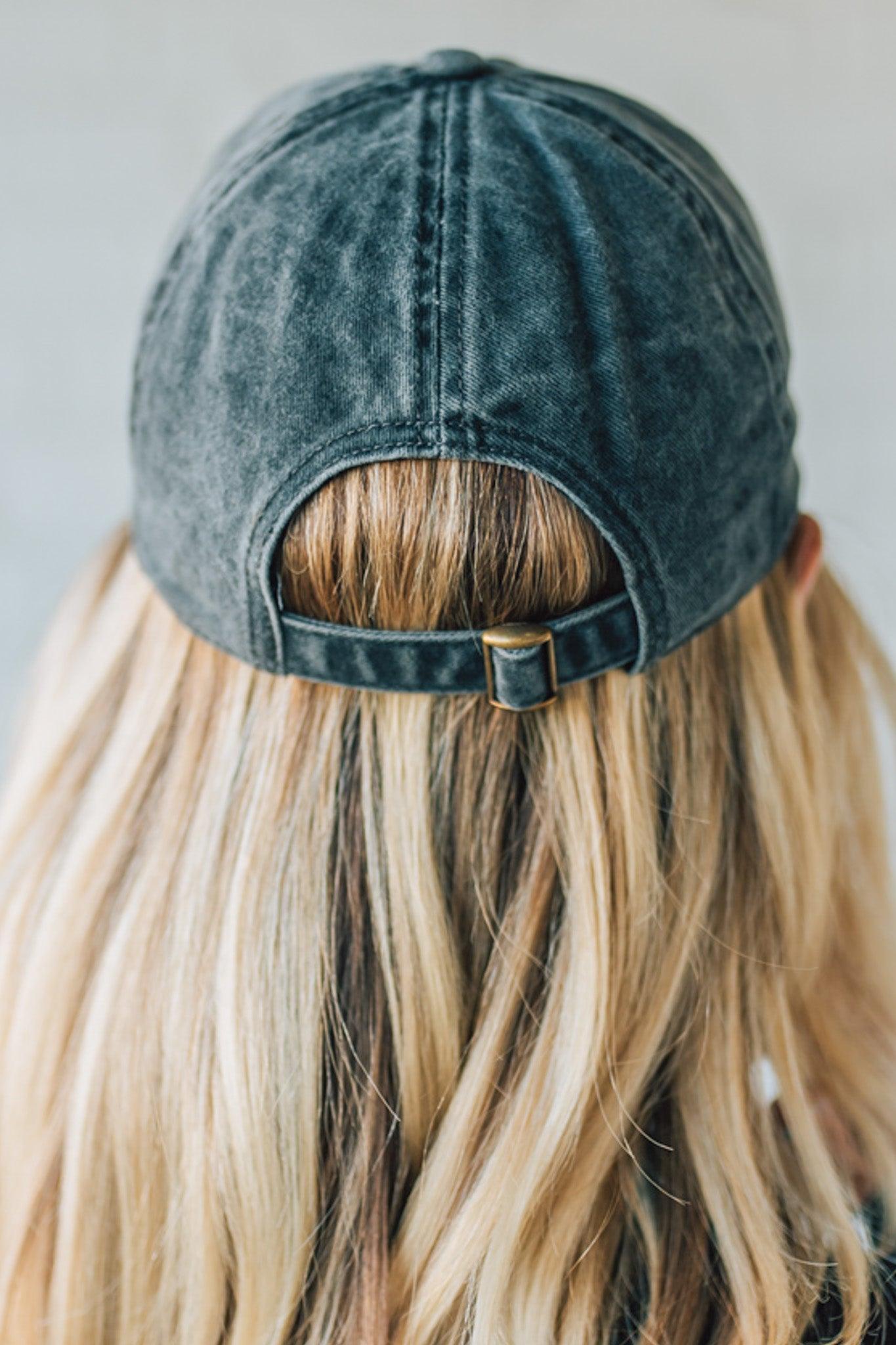 Person wearing a black distressed baseball cap with blonde hair peeking out from under it.