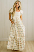 Woman wearing a floral dress standing against a wooden paneled wall.