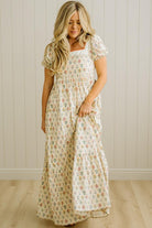 Woman wearing a floral dress standing against a plain wall.