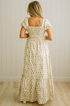 Woman wearing a floral dress standing against a white paneled wall.