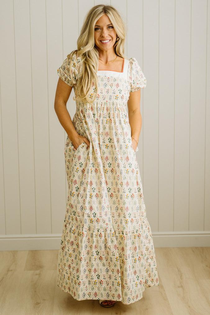 Woman wearing a floral dress standing against a white paneled wall.
