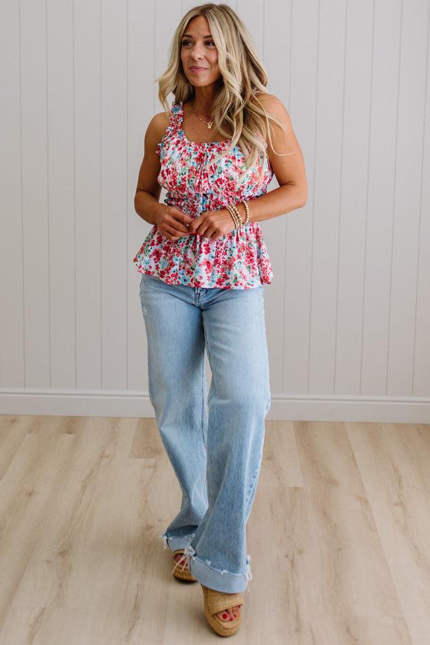Woman wearing a floral top and light blue jeans standing on a wooden floor.