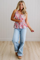 Woman wearing a floral top and jeans standing against a light wooden paneled wall.