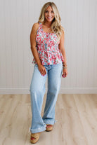 Woman wearing a floral top and light blue jeans standing against a white paneled wall.