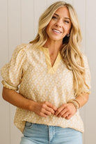 Woman wearing a yellow patterned blouse with blue jeans against a white wall