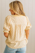 Woman wearing a yellow floral blouse and blue jeans against a white wall.