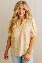 Woman wearing a yellow patterned blouse against a light wooden panel background