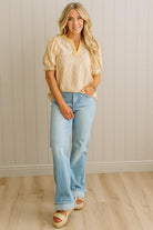 Woman wearing a yellow blouse and light blue jeans standing against a beige wall.