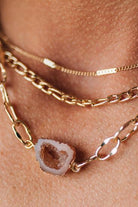 Close-up of a person wearing gold chain necklace with a central stone on a skin background