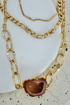 Gold chain necklaces with a central brown stone on a textured surface
