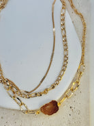 Three gold chain necklaces on a light stone surface