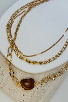 Three gold chains stacked on a textured white surface