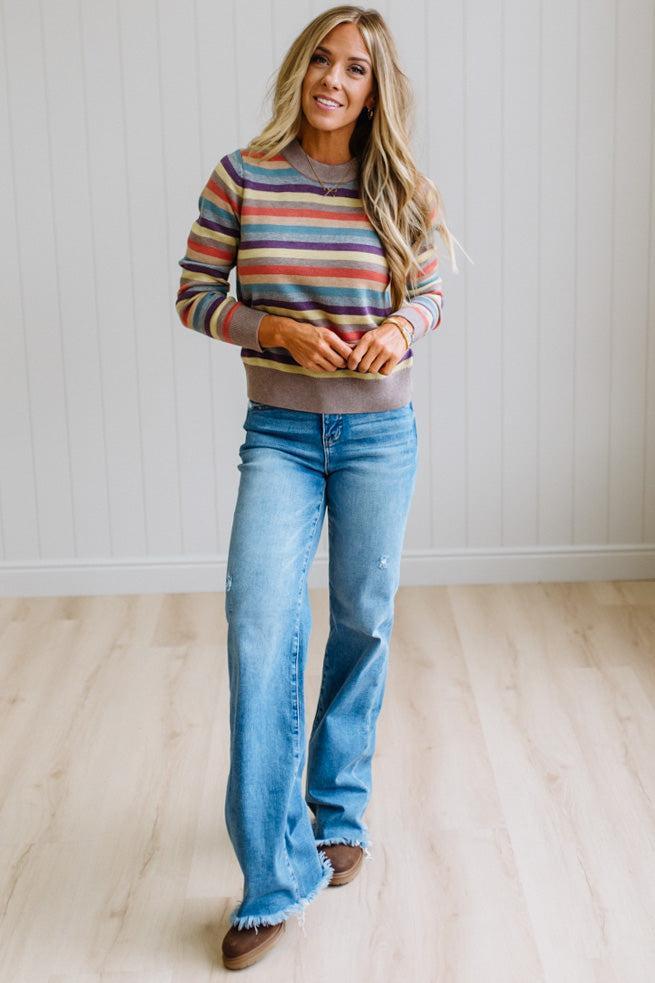 Blonde Woman Modeling a Wool Blended Multi Color Stripe Sweater Standing on a Light Wood Floor with Cream Backdrop.