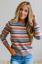 Blonde Woman Modeling a Wool Blended Multi Color Stripe Sweater Standing on a Light Wood Floor with Cream Backdrop.