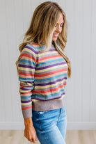 Blonde Woman Modeling a Wool Blended Multi Color Stripe Sweater Standing on a Light Wood Floor with Cream Backdrop.