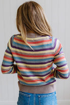 Blonde Woman Modeling a Wool Blended Multi Color Stripe Sweater Standing on a Light Wood Floor with Cream Backdrop.