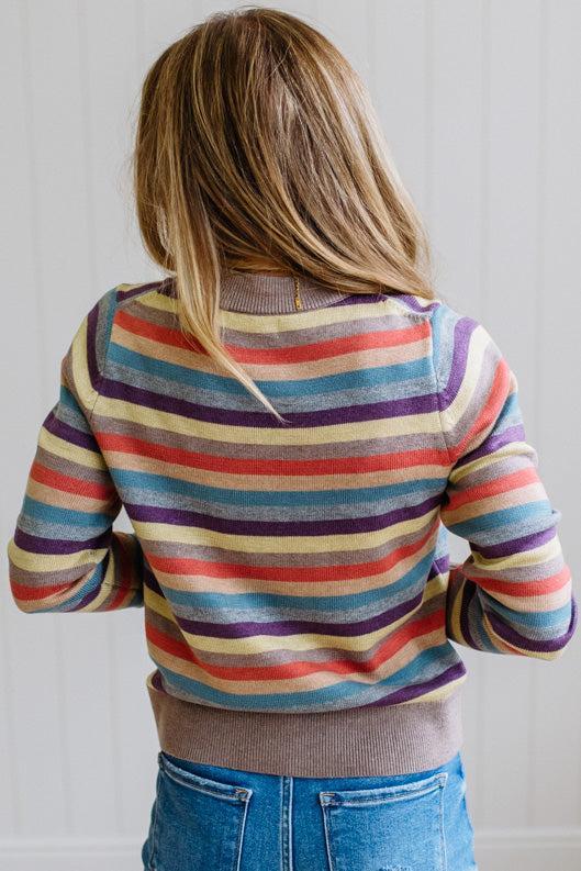 Blonde Woman Modeling a Wool Blended Multi Color Stripe Sweater Standing on a Light Wood Floor with Cream Backdrop.
