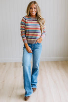 Blonde Woman Modeling a Wool Blended Multi Color Stripe Sweater Standing on a Light Wood Floor with Cream Backdrop.