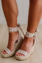 Woman wearing a mocha and cream gingham print wrap wedge sandals.