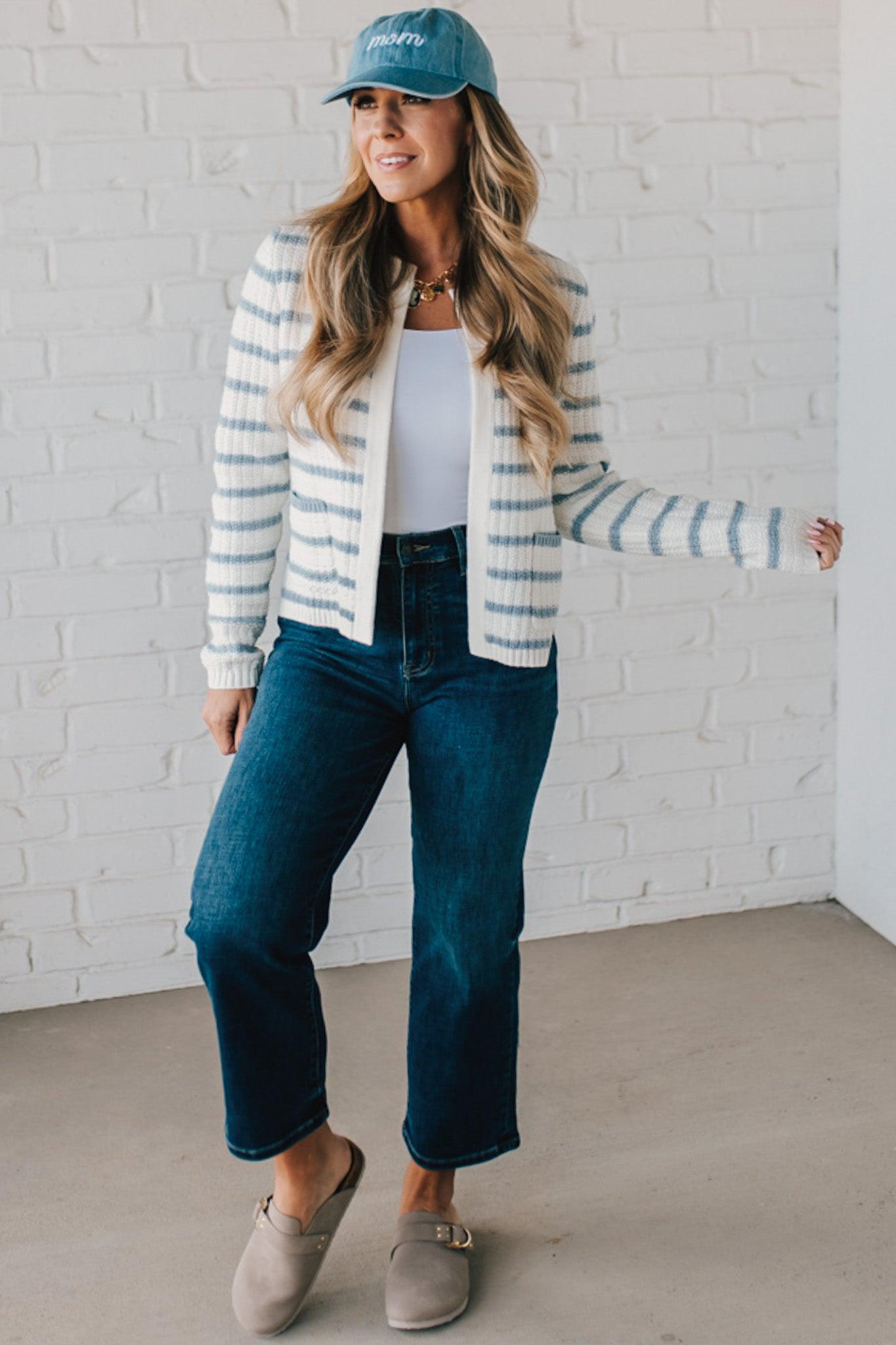 Blonde woman in a denim hat wear a cream and blue striped sweater cardigan with pockets