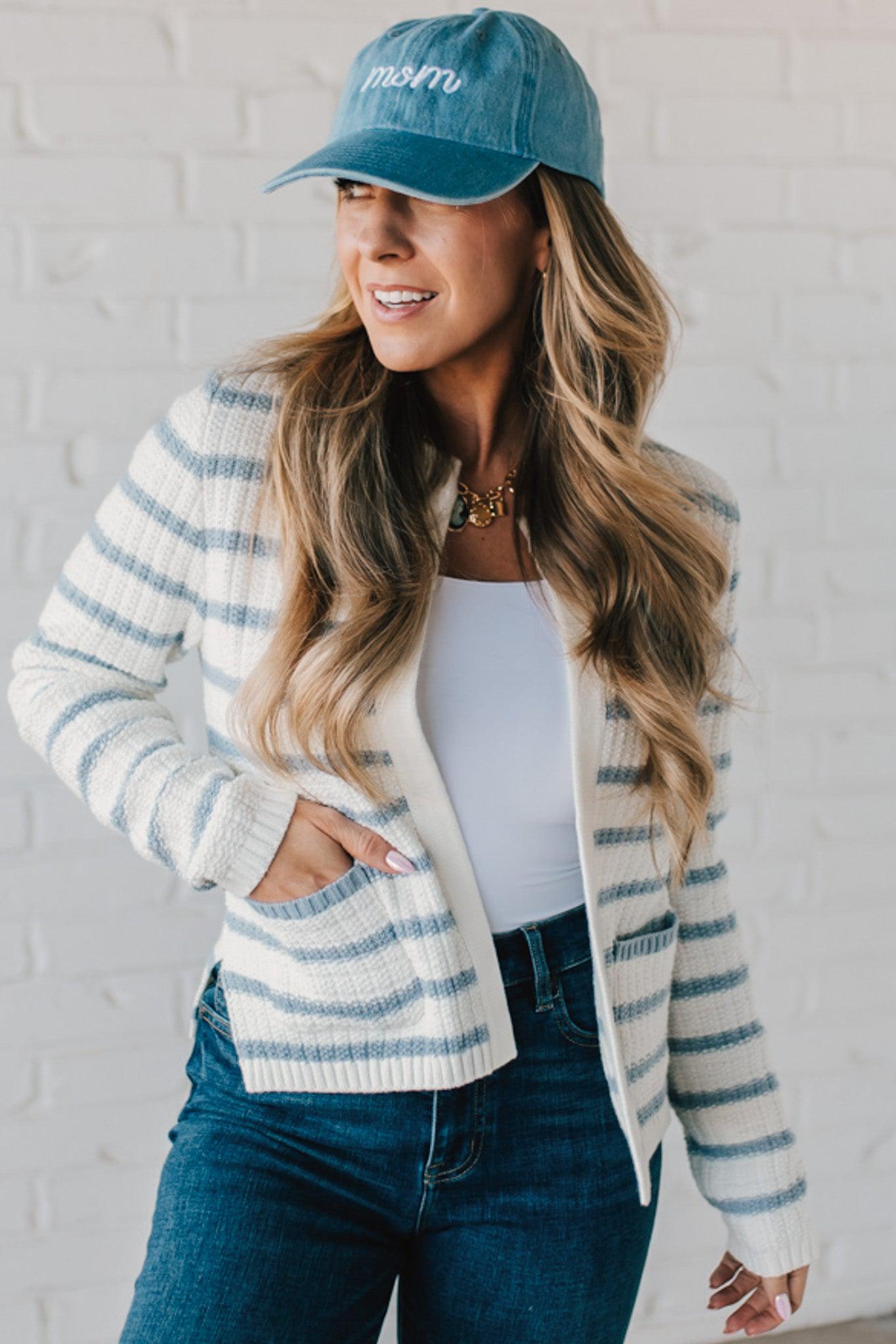 Blonde woman in a denim hat wear a cream and blue striped sweater cardigan with pockets