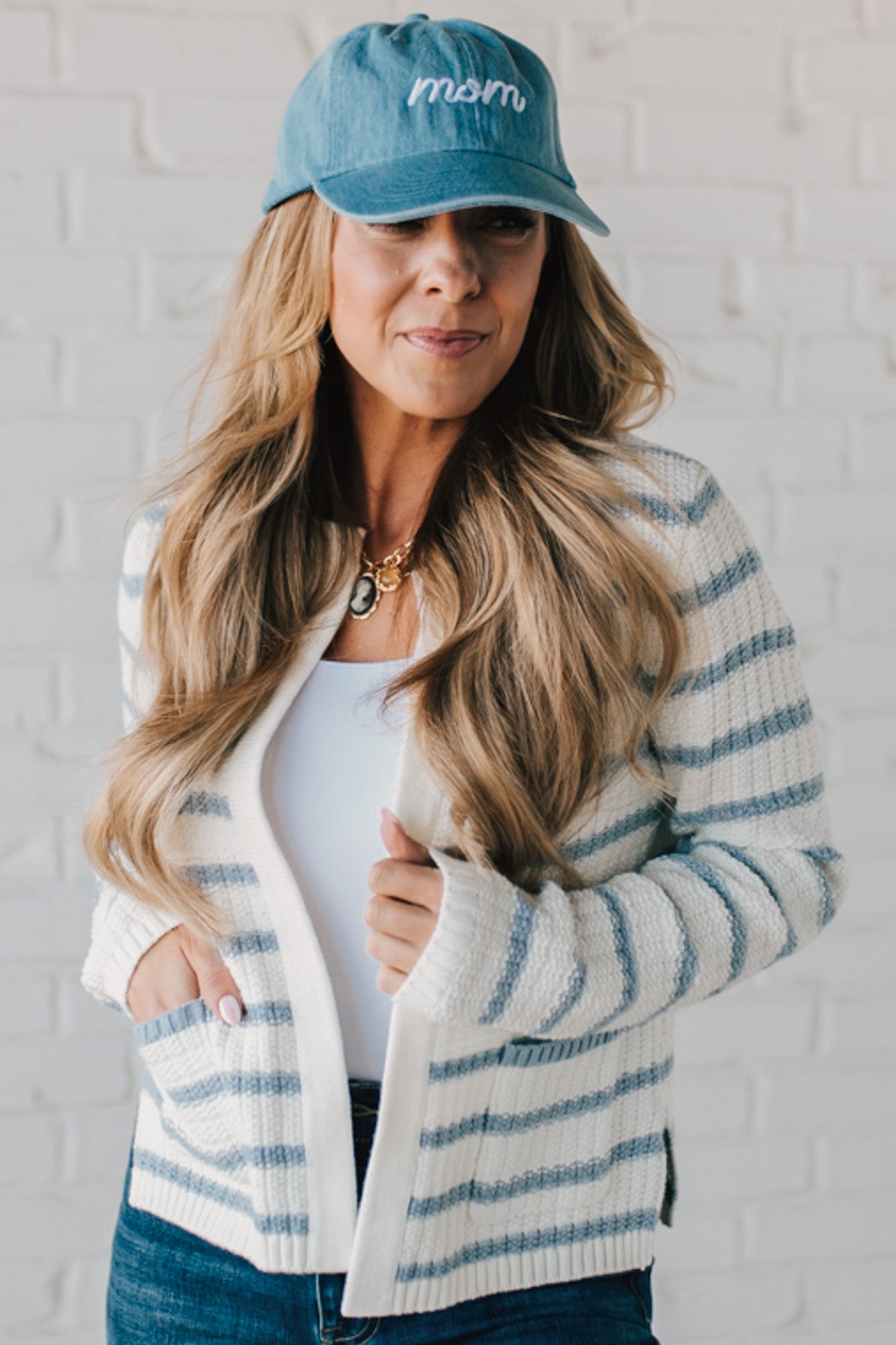 Blonde woman in a denim hat wear a cream and blue striped sweater cardigan with pockets