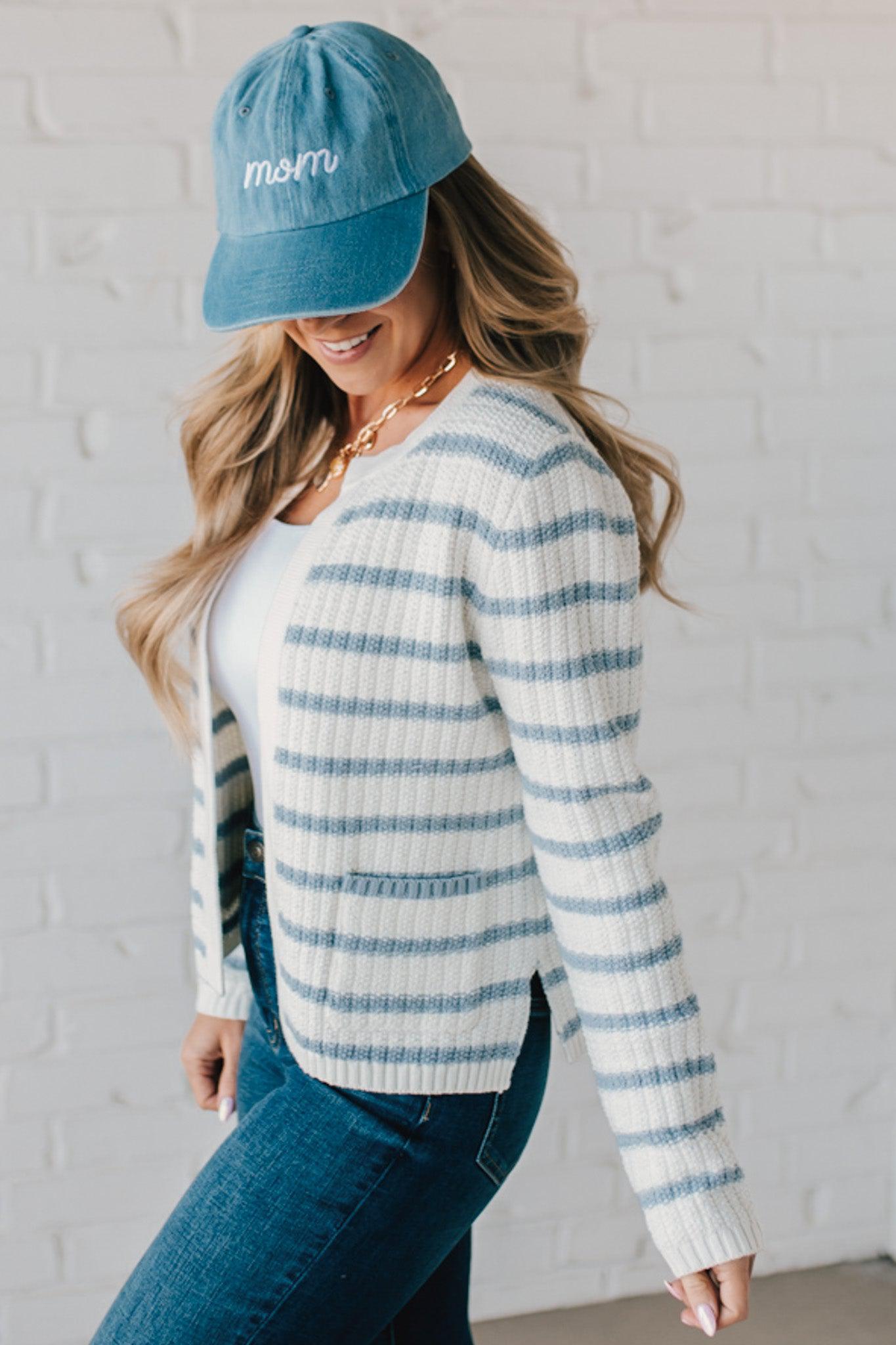 Blonde woman in a denim hat wear a cream and blue striped sweater cardigan with pockets