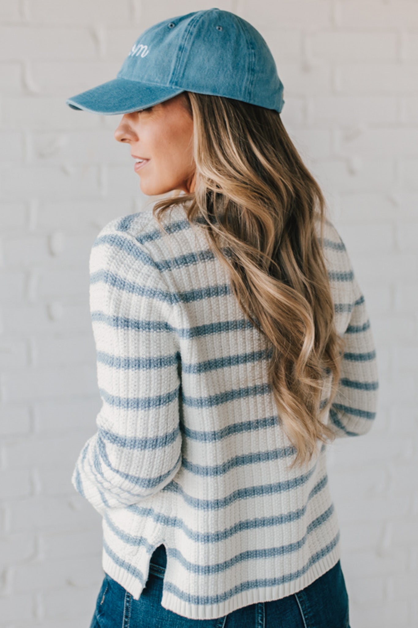 Blonde woman in a denim hat wear a cream and blue striped sweater cardigan with pockets