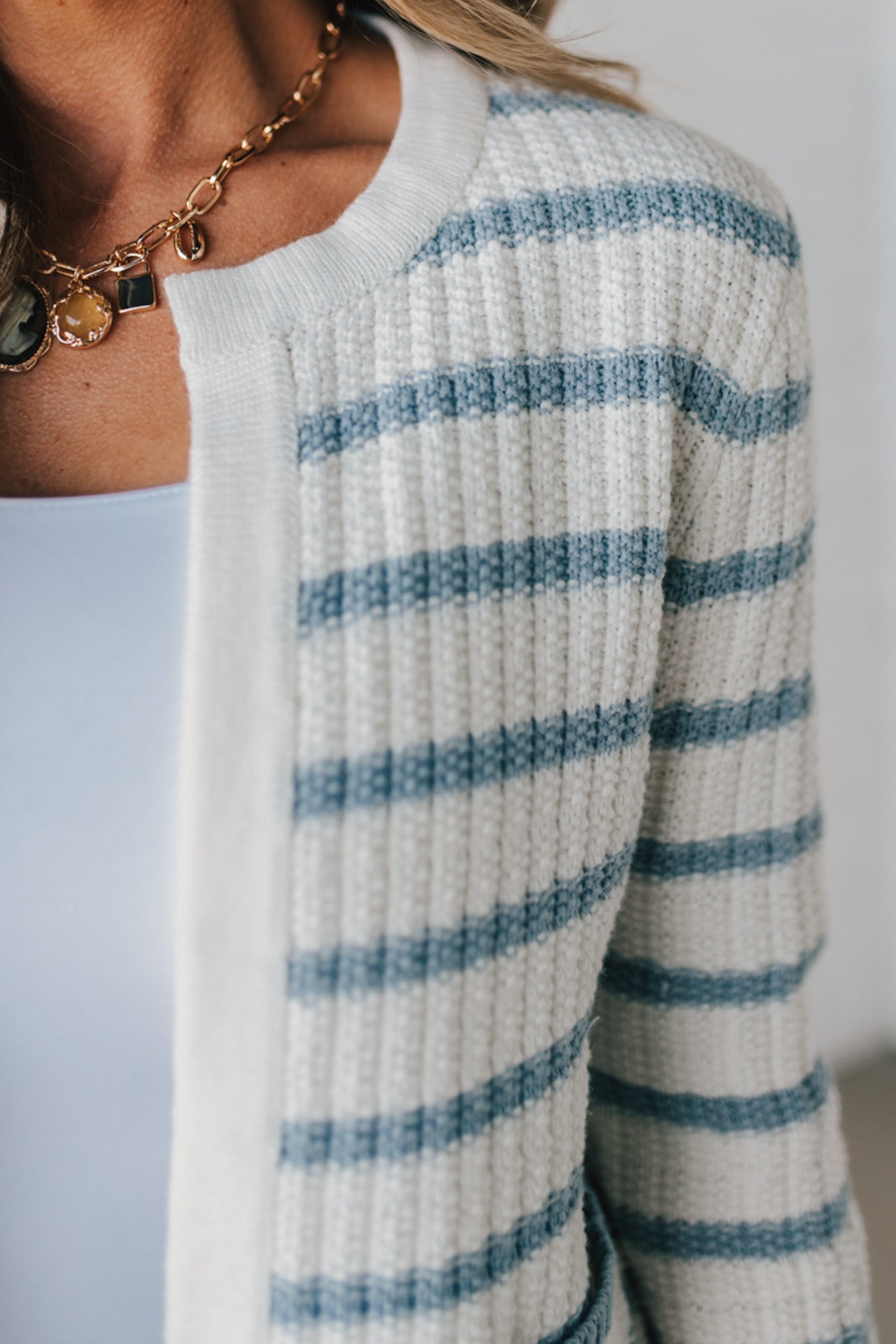 Blonde woman in a denim hat wear a cream and blue striped sweater cardigan with pockets