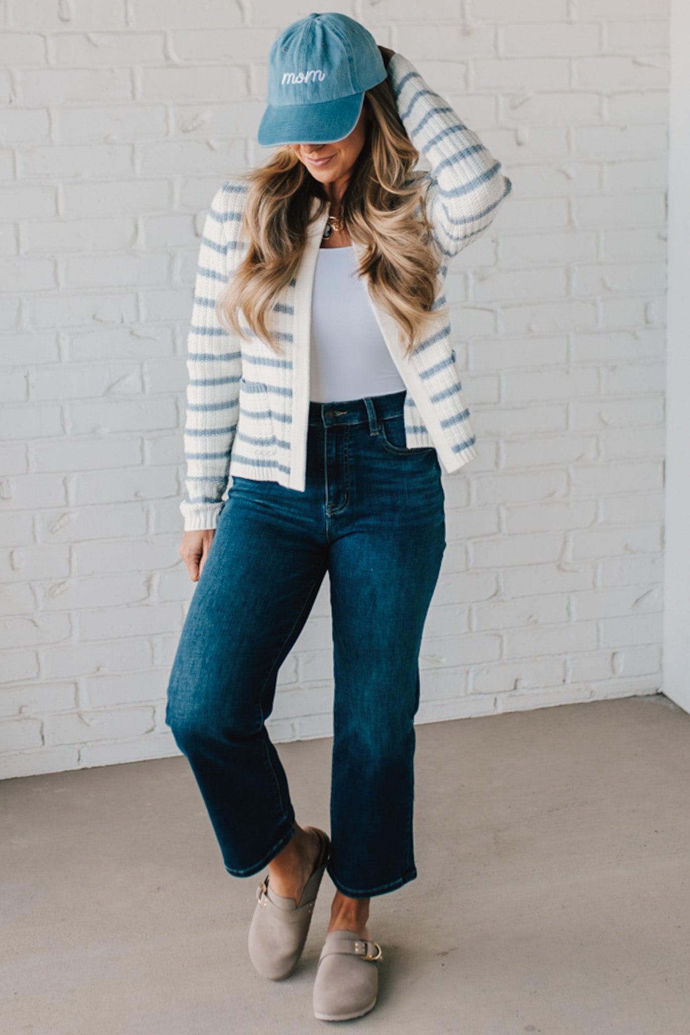 Blonde woman in a denim hat wear a cream and blue striped sweater cardigan with pockets