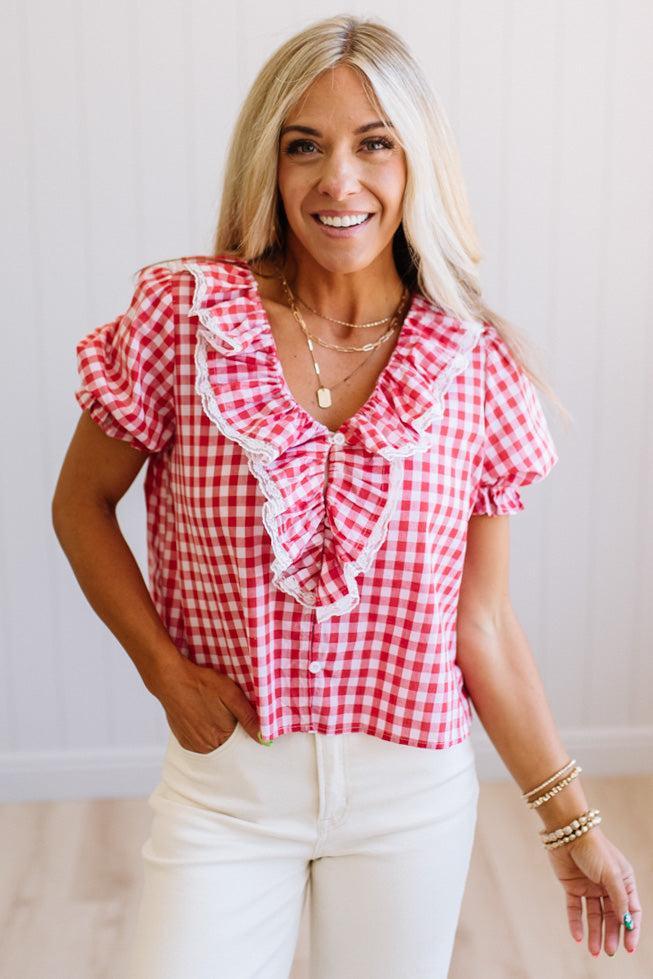 Woman wearing a red and white checkered blouse with ruffled sleeves against a plain background