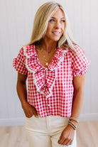 Woman wearing a red and white checkered blouse with ruffles, standing against a plain background.