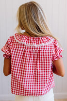 Person wearing a red and white checkered blouse with ruffled sleeves against a plain background