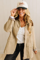 Woman wearing a beige jacket, white cap, and black pants indoors.