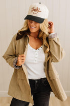 Woman wearing a beige jacket, white shirt, black pants, and a cap with 'Howdy' on it.
