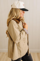 Woman wearing a beige coat and cap with a checkered shirt, standing against a neutral background