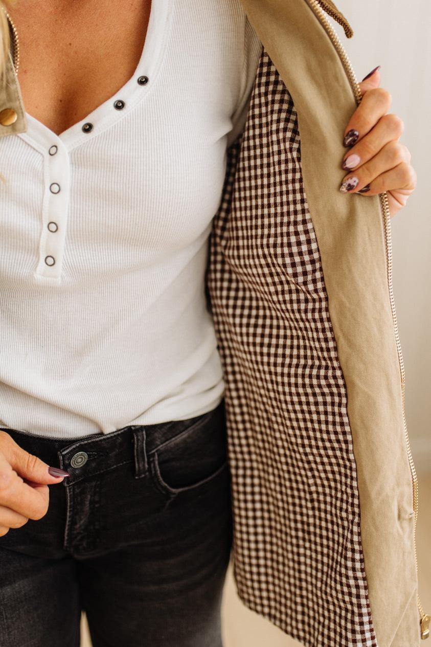 Close-up of a person wearing a white shirt, black pants, and a beige jacket with a plaid lining.