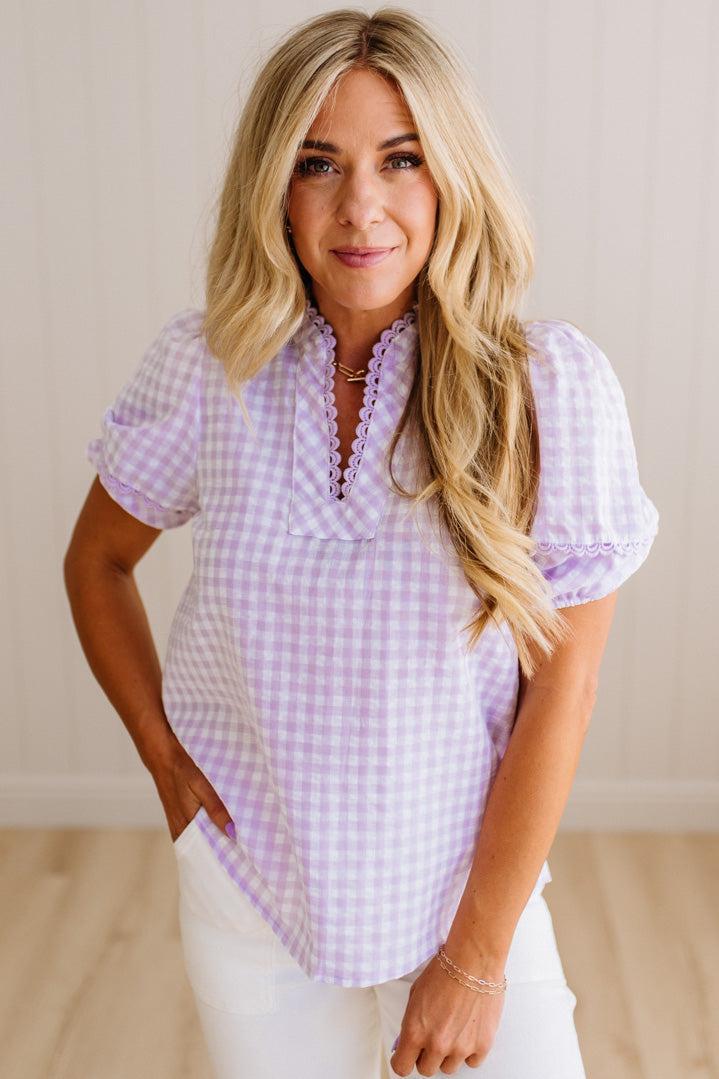 Blonde woman wearing a lavender and white gingham top with scallop edge trim and puff sleeves.