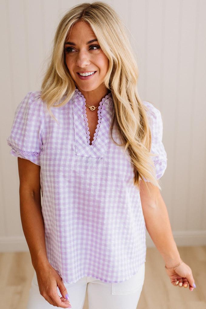 Blonde woman wearing a lavender and white gingham top with scallop edge trim and puff sleeves.