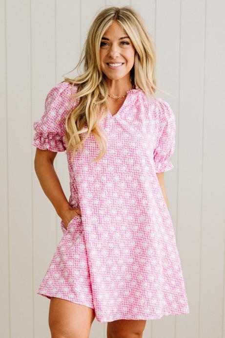 Woman wearing a pink checkered dress against a light wooden panel background