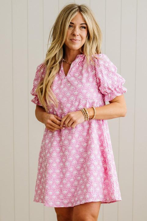 Woman wearing a pink checkered dress against a wooden panel background
