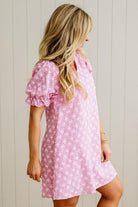 Woman wearing a pink checkered dress against a light wooden panel background