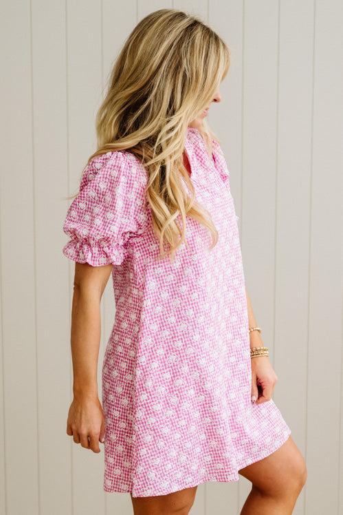 Woman wearing a pink checkered dress against a light wooden panel background